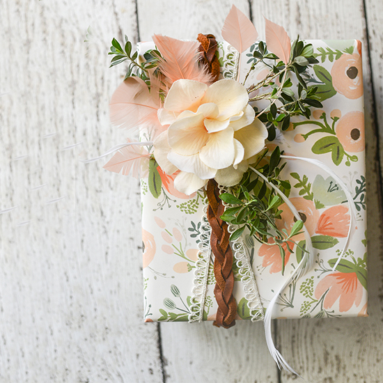 Boho inspired gift wrapping tutorial, using mixed materials, including leather, lace, feathers, flowers, and real greenery.