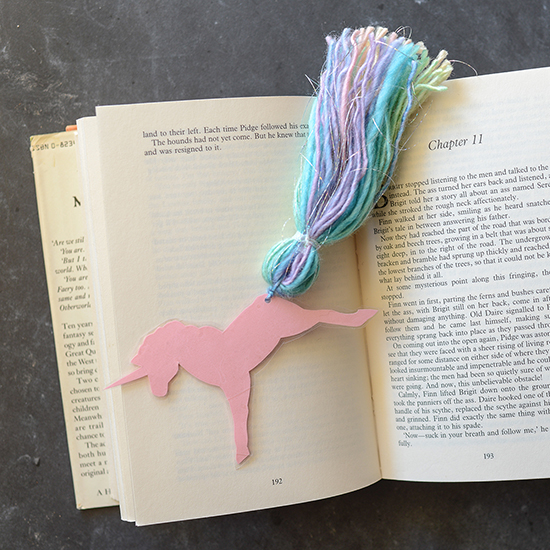 Make an enchanting unicorn bookmark using cardstock, tape, and rainbow yarn.